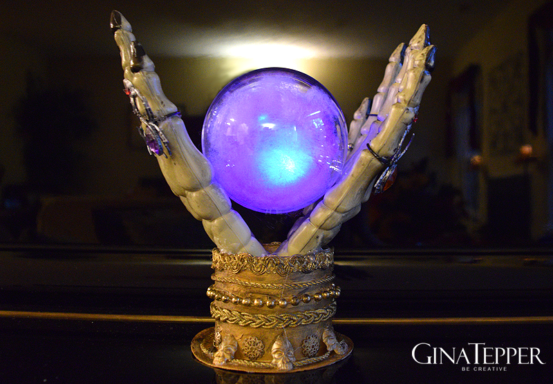Skelleton hands holding a glowing purple crystal ball in a stand