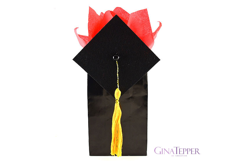 Black graduation cap with gold tassel attached to a black gift bag