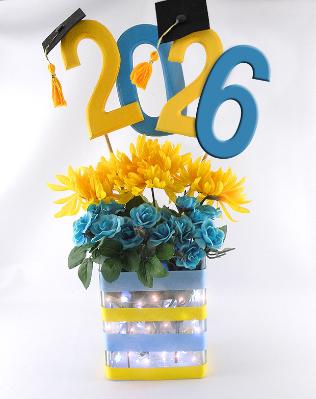 Graduation centerpiece with large 2026 numbers, graduation caps, and yellow and blue flowers with lights.