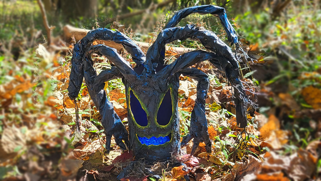 Creepy paper blue Halloween tree with yellow glowing eyes and mouth with twisted branches and hands on two of the branches,
