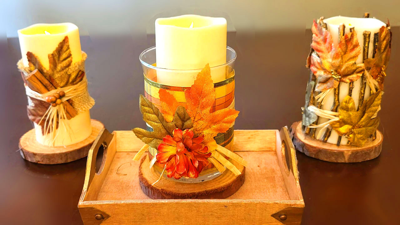 Three rustic DIY fall candles sit on a wooden tray. One is wrapped in cinnamon sticks, another has a plaid ribbon and autumn leaf, and the third is decorated with twigs and gold leaves, creating a cozy autumn scene.