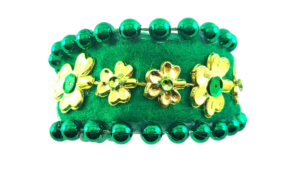 A DIY St. Patrick’s Day cuff bracelet made from vibrant green felt. The top and bottom edges are trimmed with green metallic beads, and the center features a row of gold shamrocks with green sequin centers, showcasing a high-end design.