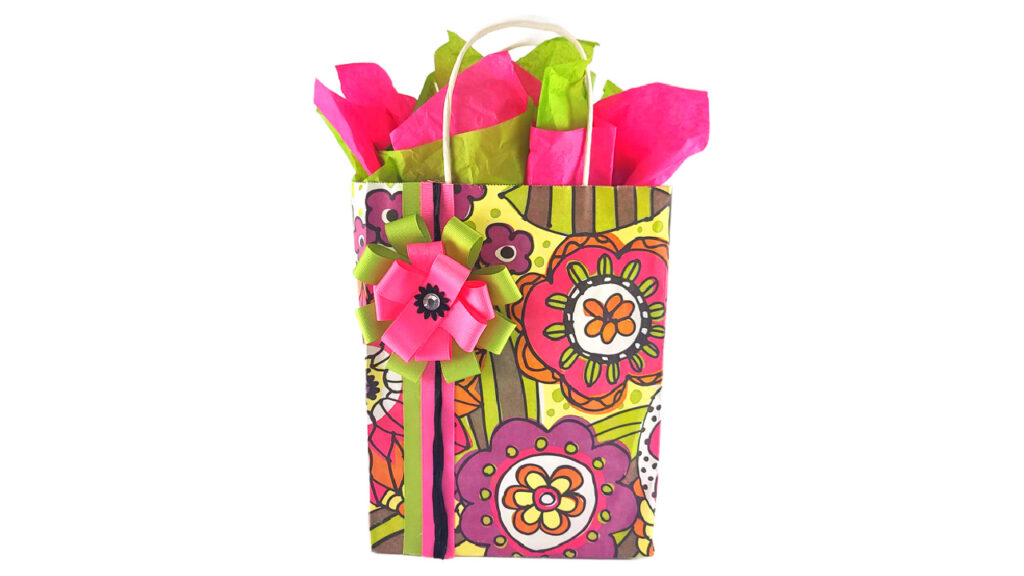 Boutique-style DIY gift bag featuring bright floral patterned paper, pink and lime green tissue paper bouquet, and custom ribbon embellishments.
