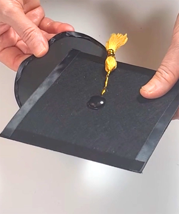 Hands holding a graduation cap with yellow tassel for DIY graduation party decor.