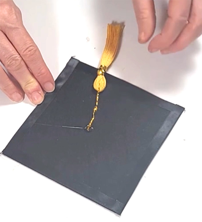 Attaching a gold tassel to a black graduation cap for DIY graduation party decor.