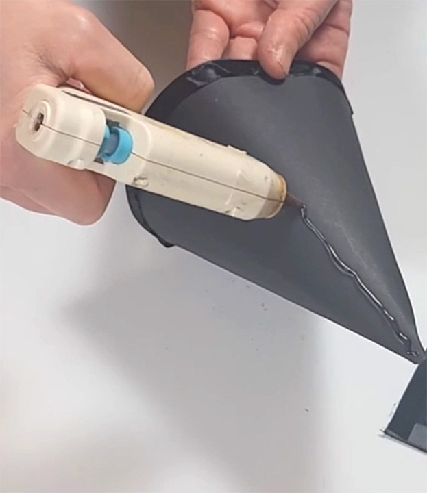 Applying hot glue to assemble a graduation hat for DIY graduation party decor.