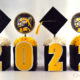 Cubes with on the front of the boxes and alternating black graduation hats with yellow tassels and school mascot