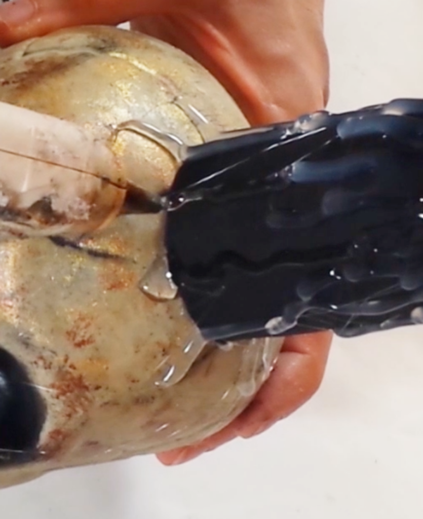 Hands dripping hot glue onto a paper tube and skull to create faux wax drips for a DIY Halloween candle.