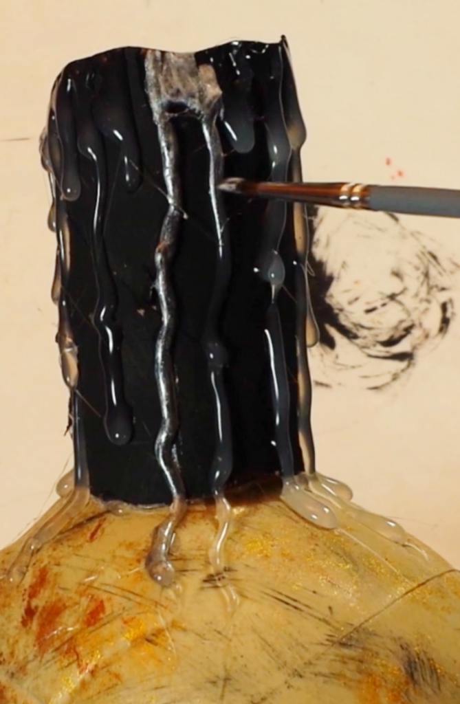 Paintbrush applying silver paint to hot‑glue drips on a DIY Halloween candle to create an aged, ashed‑over look.