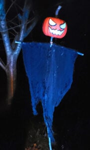 Hanging haunted scarecrow pumpkin figure with glowing eyes and mouth, draped in tattered cloth outdoors at night.