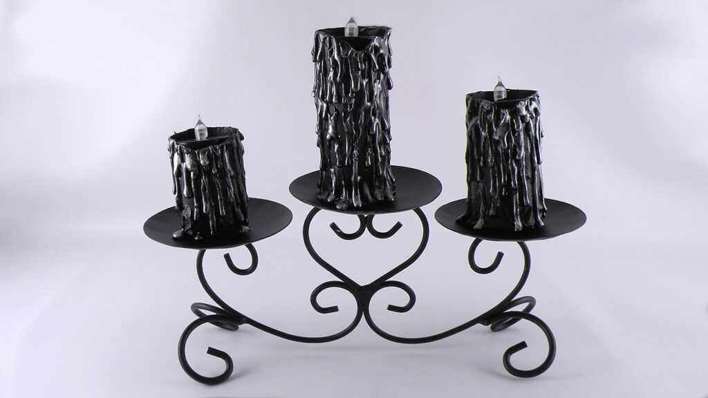 Black faux wax‑dripped candles displayed on a wrought‑iron candle stand for gothic Halloween decor.