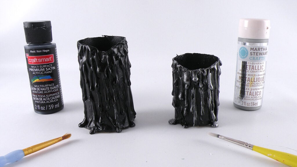 Black acrylic paint and silver craft paint beside paper towel roll candle bases being painted for a DIY Halloween candle project.