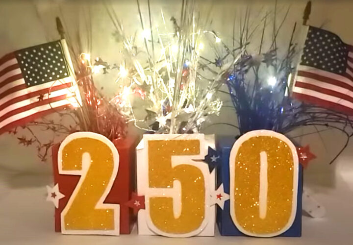 Patriotic July 4th centerpiece featuring glittery “250” numbers, American flags, and red, white, and blue streamers arranged on a festive display.