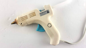 A perfectly clean, white mini hot glue gun sitting on a white background after using the aluminum foil cleaning hack.