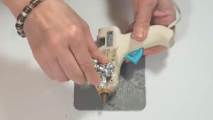 Using a crumpled piece of aluminum foil to gently scrape the burnt, sticky residue off the side of a warm hot glue gun.