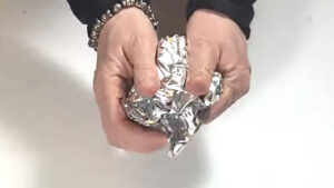 Crumpling a sheet of aluminum foil into a tight ball to create a scraping tool to clean a hot glue gun.