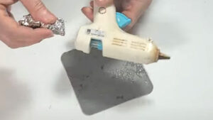 Carefully rubbing the metal nozzle of a warm mini hot glue gun with aluminum foil to easily remove dried, stuck-on glue.