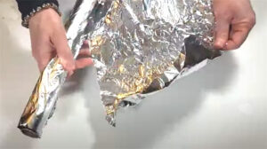Tearing off a fresh sheet of aluminum foil from the roll to use for cleaning the hot glue gun.