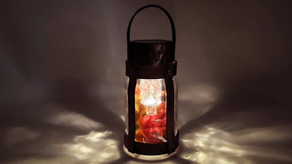 Industrial mason jar solar lantern glowing at night with fall leaves creating patterns of light